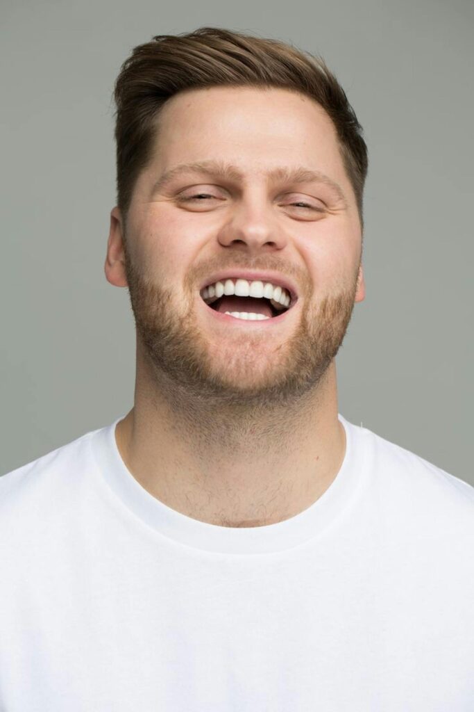 Portrait of a happy man laughing, wearing a white t-shirt, isolated on gray background.