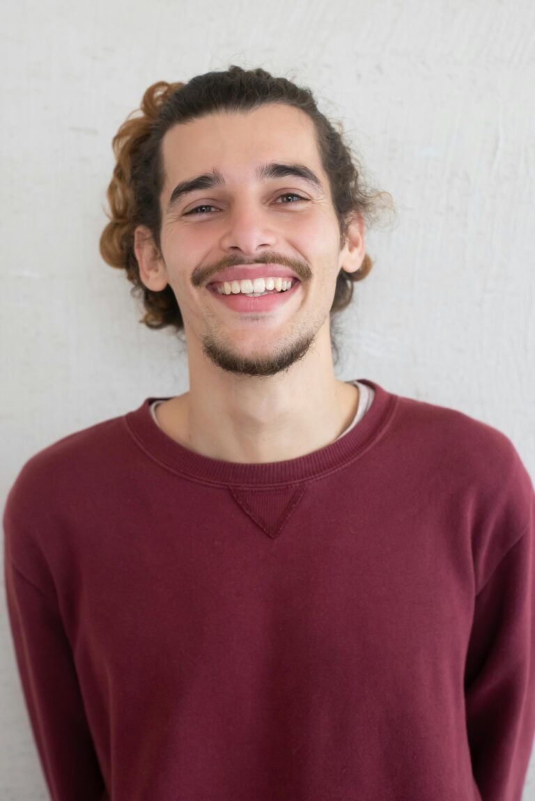 Portrait of a young man with a goatee smiling warmly in a burgundy sweater.